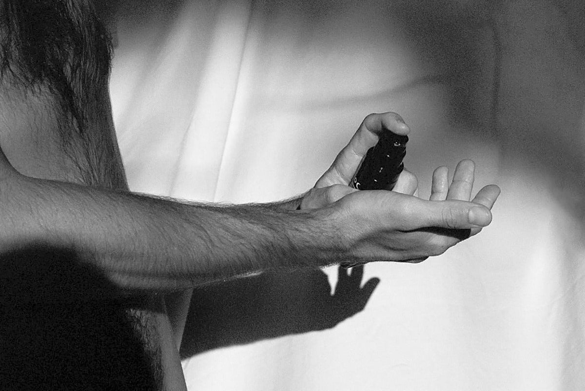 Black-and-white study of two hands dispensing product from a small bottle — skincare for men