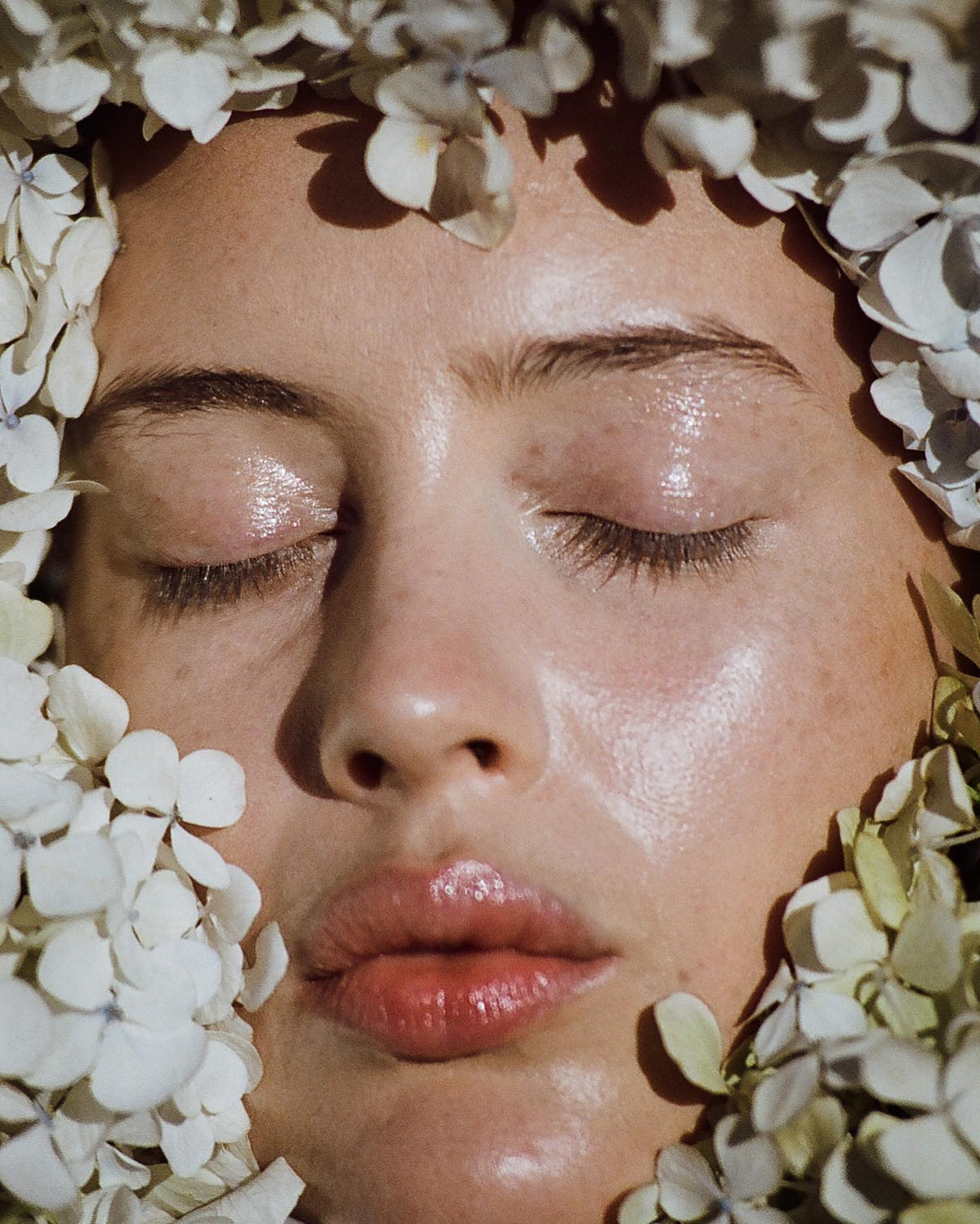 Woman with her eyes closed framed by white hydrangea blooms, skin dewy — plump, hydrated skin article