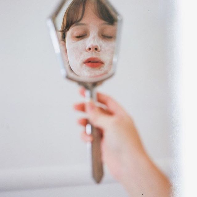 Woman holding a hand mirror reflecting her face, eyes closed — vitamin A alternatives in pregnancy