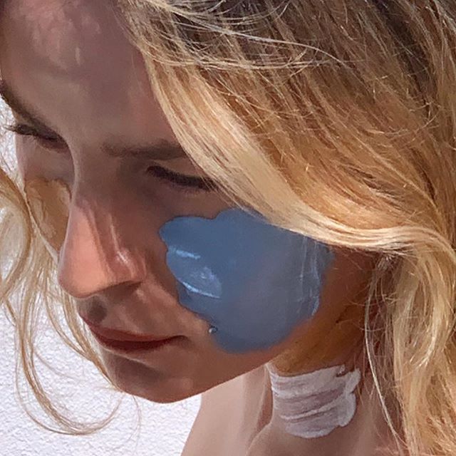 Woman with blonde hair and a blue masque patch on her cheek, looking down — fillers article