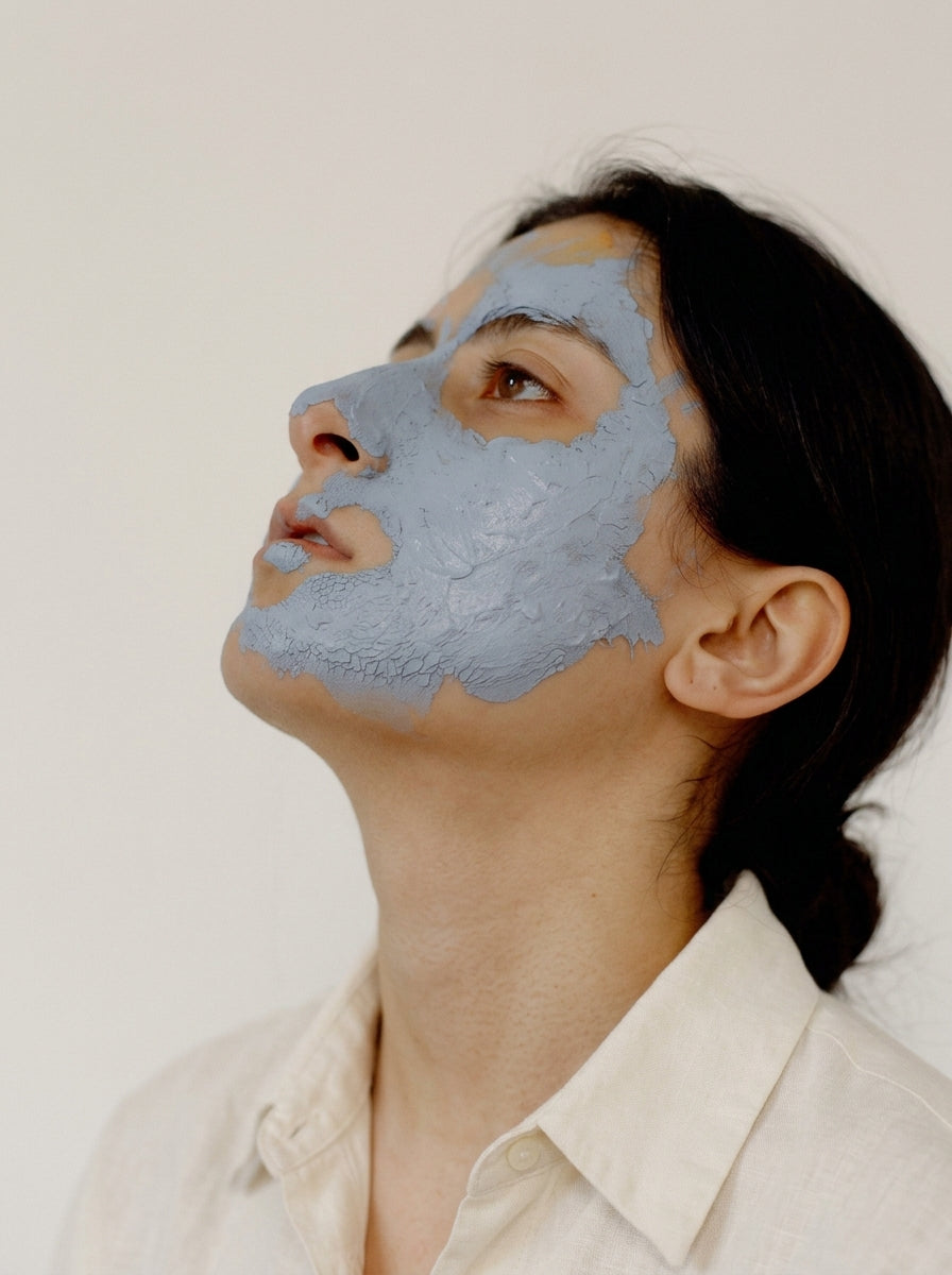 Woman looking upward wearing a blue-grey clay masque on one side of the face — Aliangé breakout protocol