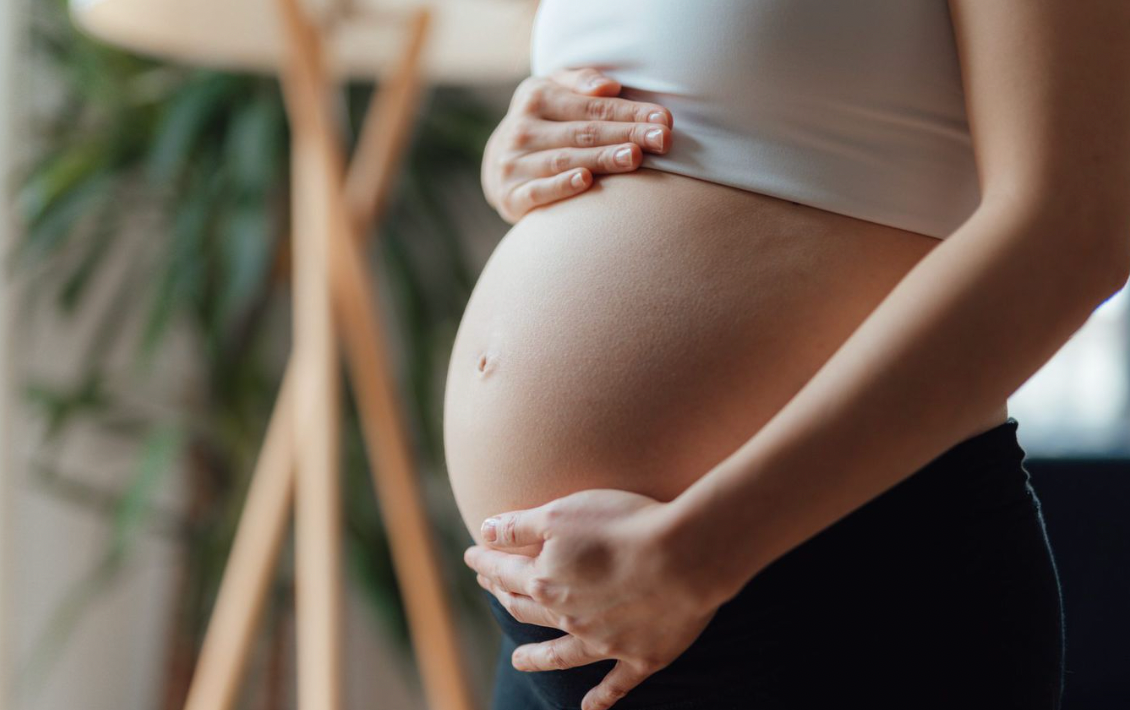 Pregnant woman cradling her bump in a bright room — pregnancy and skincare article