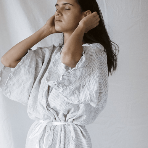 Woman in a white pinstriped robe with her hands behind her head, eyes closed — UV and DNA repair article